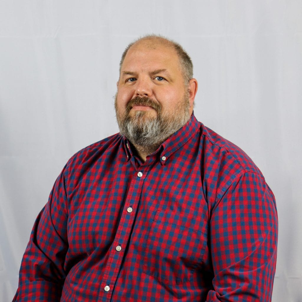 White male with a neatly kept beard wearing a maroon and blue checkered shirt.