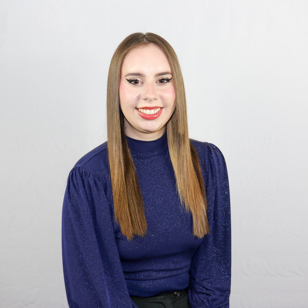White female with long, straight light brown hair, wearing a blue shirt.