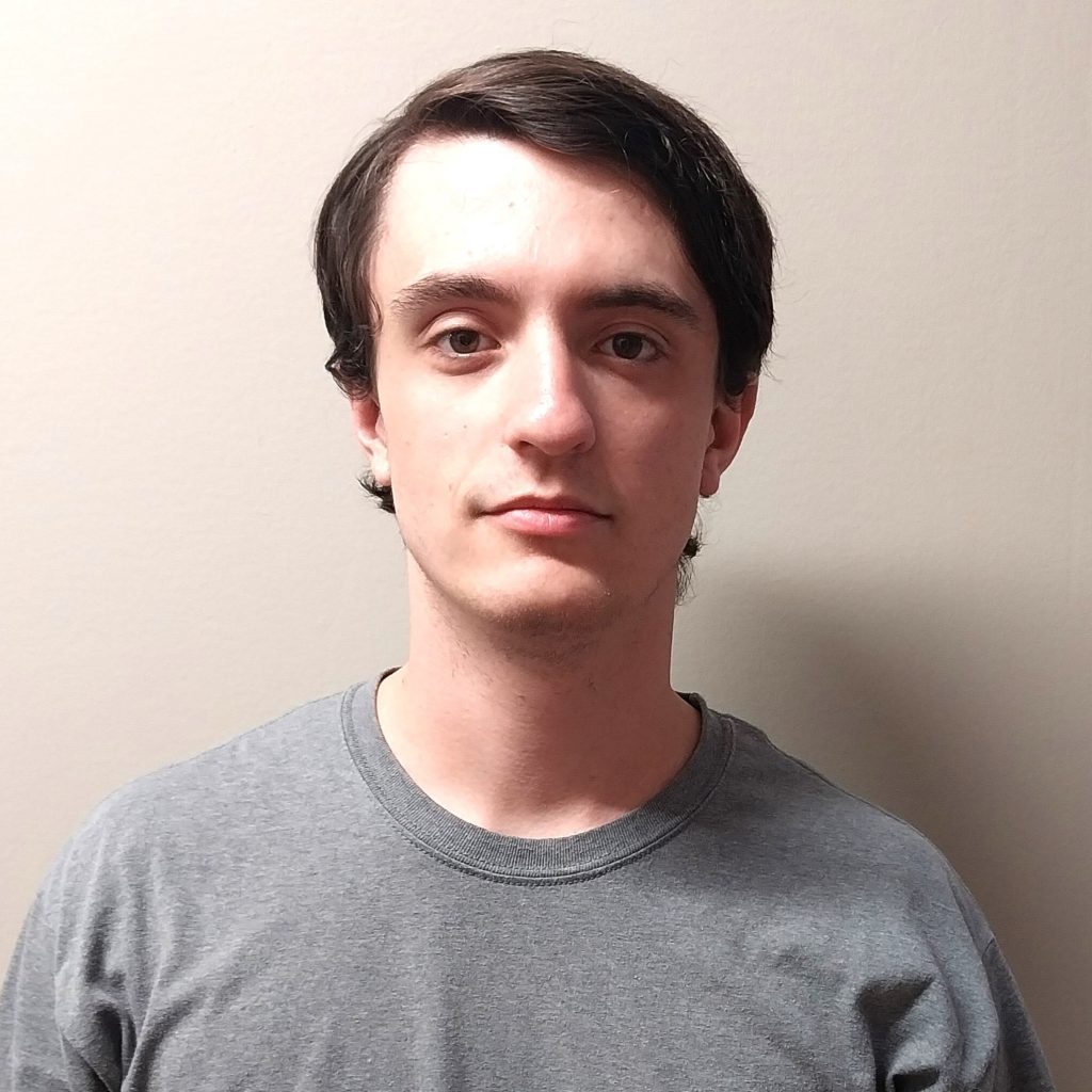 White male with slicked back brown wearing a grey shirt