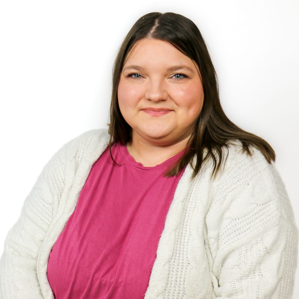 white female with shoulder length straight brown hair wearing a Pink shirt and white sweater