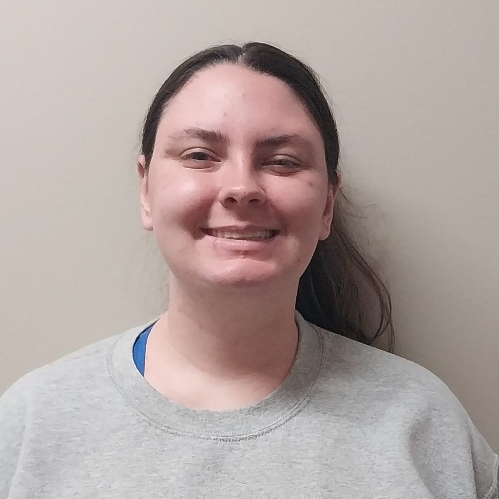 White female with pulled back brown hair a grey shirt.