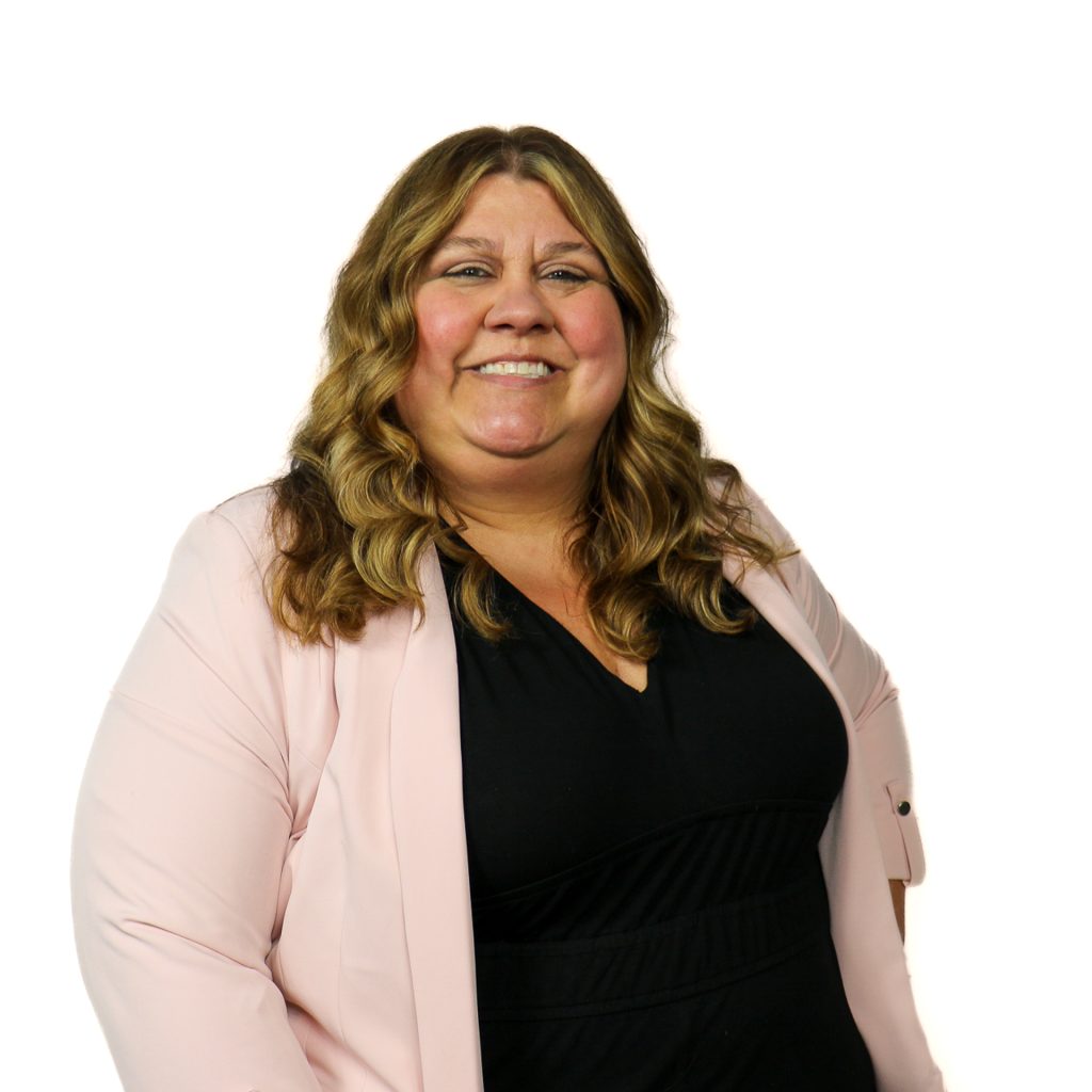 White female with wavy light brown and blonde hair wearing a black top and light pink blazer