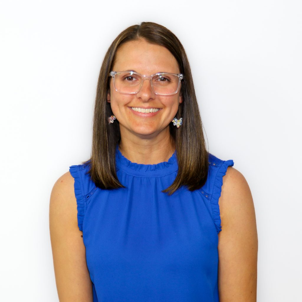 White female smiling with brown straight shoulder length hair and glasses in a blue shirt