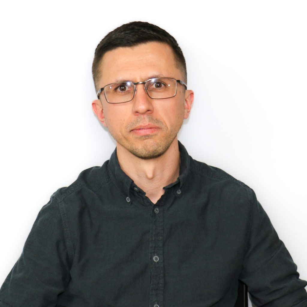 White male with rectangular eyeglasses wearing a black button up shirt.