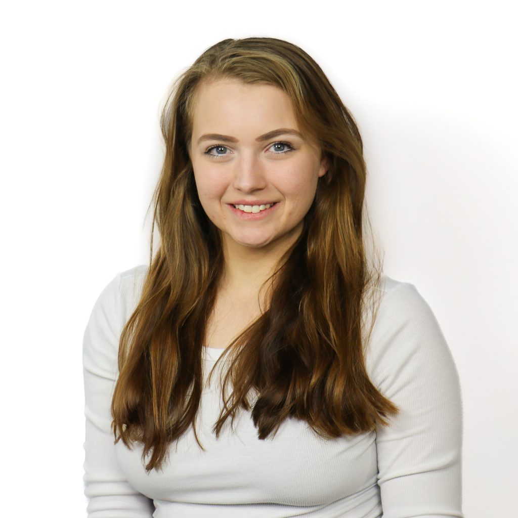 White female with long wavy brown hair wearing a white top