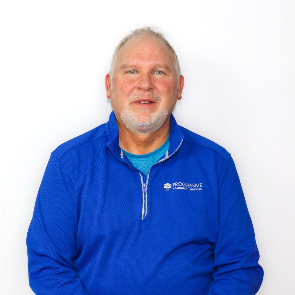 White male with short grey/blonde hair, and a neatly trimmed grey goatee wearing a blue ¼ zip pullover jacket.