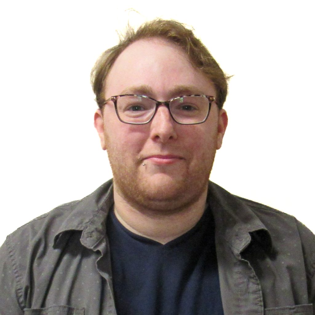 White male with short blonde hair, wearing rectangular eyeglasses, a blue shirt and grey jacket.